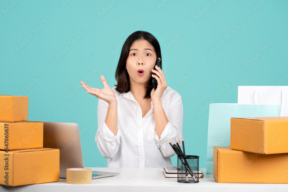 Shocked businesswoman talks to a customer on a smartphone with a brown cardboard parcel on a pastel green background. Shocked businesswoman talks to a customer on a smartphone with a brown cardboard parcel on a pastel green background.