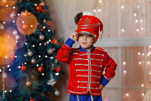 A boy in a nutcracker costume plays with the mouse symbol of the year. christmas tree and gifts