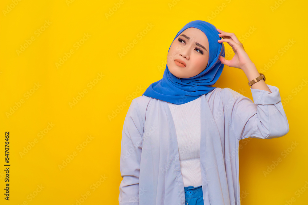 Thoughtful young Asian Muslim woman looking up at copy space, thinking and making decisions isolated on yellow background Thoughtful young Asian Muslim woman looking up at copy space, thinking and making decisions isolated on yellow background