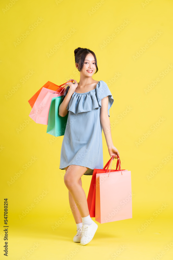image of a beautiful asian girl in a dress holding a shopping bag in her hand posing on a yellow background
