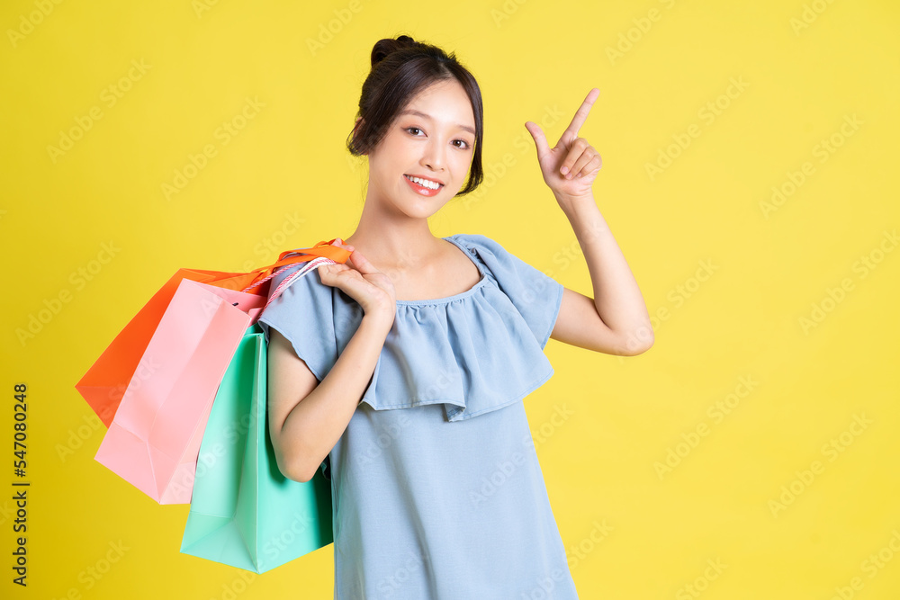 image of a beautiful asian girl in a dress holding a shopping bag in her hand posing on a yellow background image of a beautiful asian girl in a dress holding a shopping bag in her hand posing on a yellow background