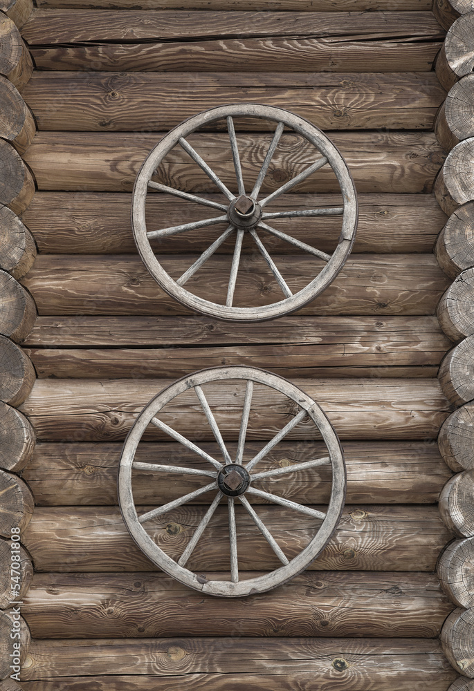 Obraz premium Two old wooden wheels fixed vertically on a log wall