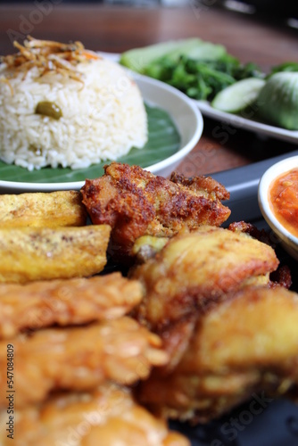 "Nasi Liwet" one of traditional food from Sunda, West Java, Indonesia. Served with vegetable or lalapan, chilli sauce, fried tempe, fried tofu and fried chicken. Wooden background.