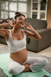 Beautiful pregnant woman practising yoga at home. Young woman listening music while exercise at home..