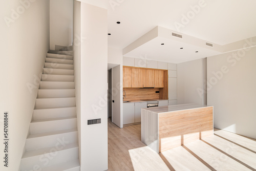 Empty interior of refurbished duplex with stairs and modern kitchen with island and wooden furniture