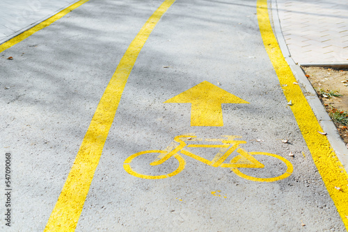 Outdoor bike path. Close-up of painted yellow bicycle sign and an arrow on pavement with stripes