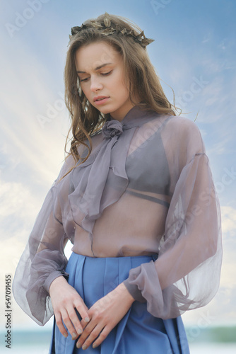 Lonely young woman on the beach in blue skirt and transparent blouse