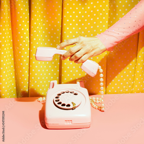 Old fashioned rotary dial telephone and female hand, creative nostalgic layout, retro aesthetic, pink and yellow background. 