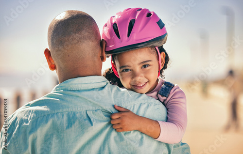 Father, bicycle and girl portrait of a young kid with a helmet by the sea ready for cycling learning. Family, holiday and fun of a dad and child hug with happiness and bike gear excited for activity