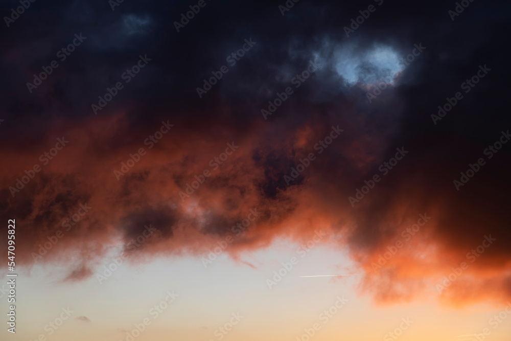 Dramatic sunset skies with orange and black clouds and a plane flying