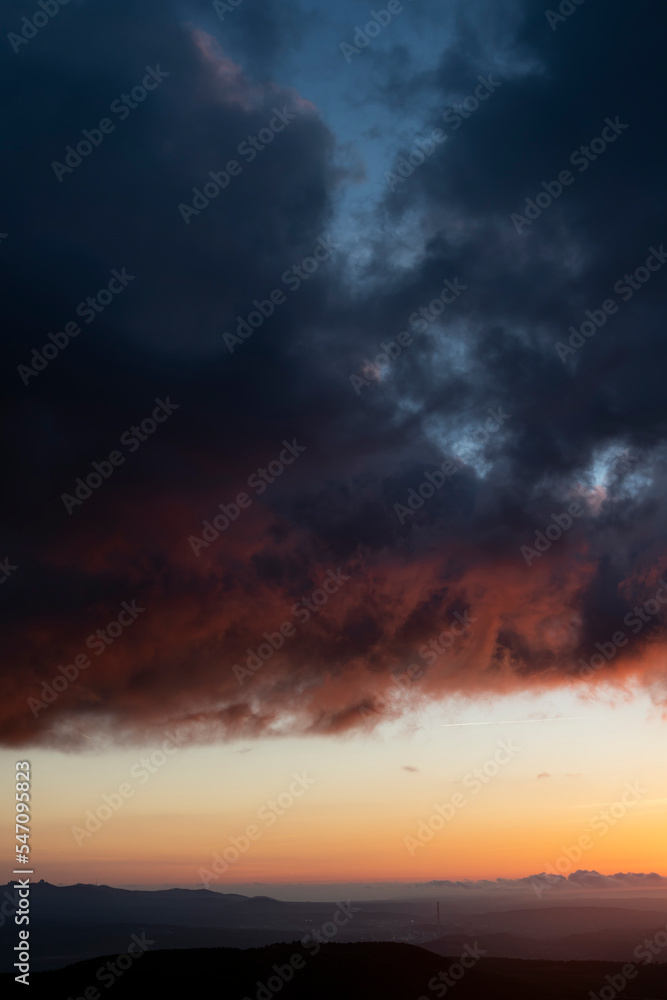 Dramatic sunset skies with orange and black clouds and a plane flying, vertical shot