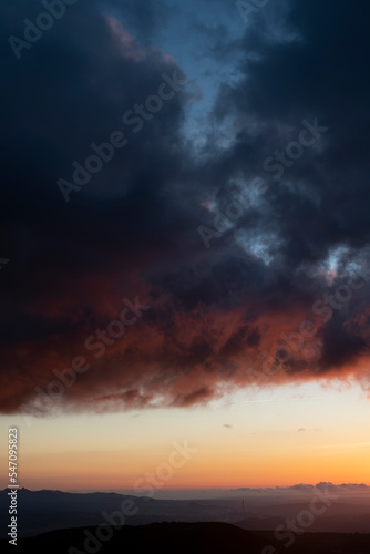 Dramatic sunset skies with orange and black clouds and a plane flying, vertical shot