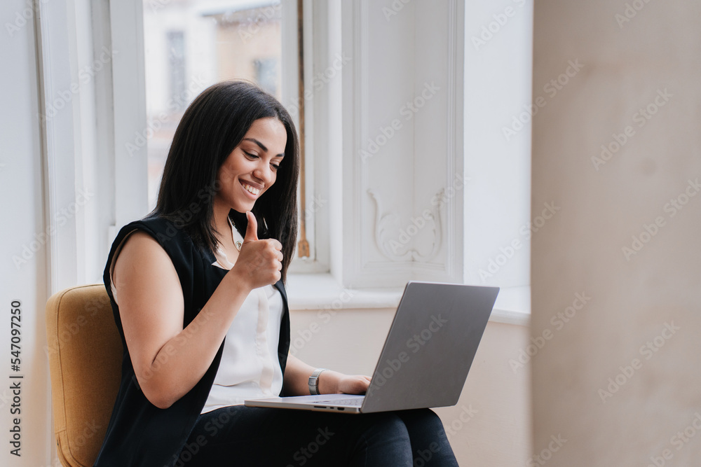 Beautiful Brazilian female student having distant lesson, using laptop sitting at home. African American businesswoman shows thumb up gesture. Pretty entrepreneur making online purchase. Beautiful Brazilian female student having distant lesson, using laptop sitting at home. African American businesswoman shows thumb up gesture. Pretty entrepreneur making online purchase.