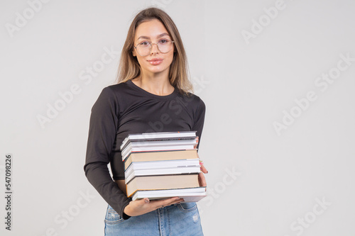 Attractive brown-haired girl in a black top and blue jeans holds a stack of books. Student with books preparing for the exam