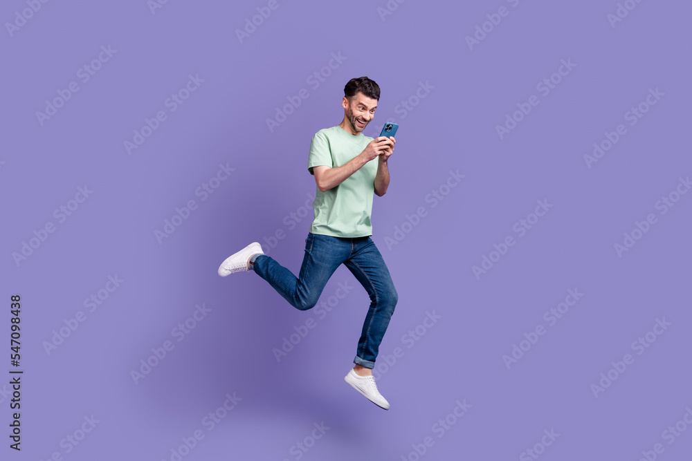 Full length photo of cheerful crazy man use modern gadget look telephone read good news isolated on purple color background Full length photo of cheerful crazy man use modern gadget look telephone read good news isolated on purple color background