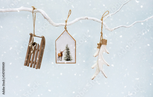 Beautiful Christmas wooden decorations hanging on tree branch, snow on blue background. Holiday mood. Hygge Home style. Merry Christmas card, New Year invitation. Copy space.