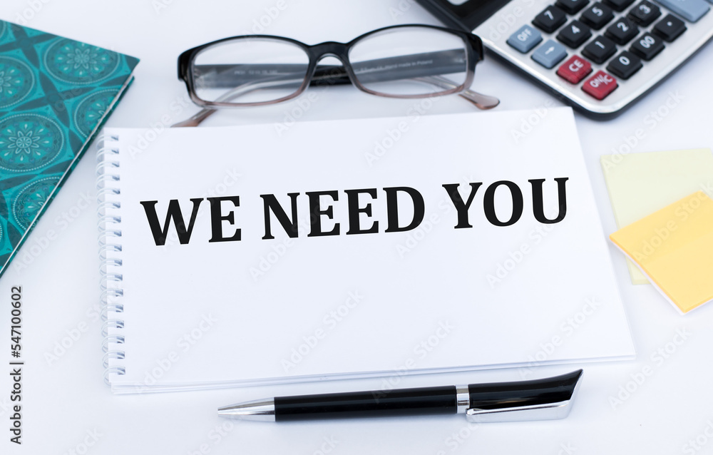 We need you text on a notebook on a desk, a business concept We need you text on a notebook on a desk, a business concept