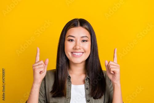 Portrait of good mood positive nice girl with long hairstyle dressed khaki shirt directing empty space isolated on yellow color background