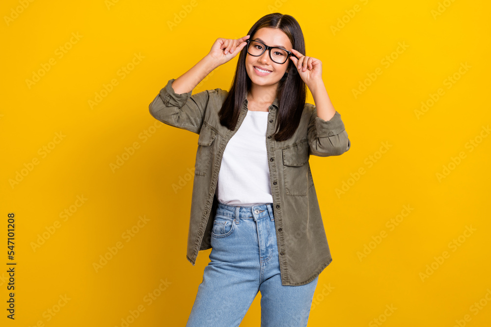 Portrait of satisfied sweet clever woman with long hairdo wear khaki shirt hands touch glasses isolated on yellow color background Portrait of satisfied sweet clever woman with long hairdo wear khaki shirt hands touch glasses isolated on yellow color background