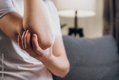 Health, arthritis of joints pain in elbow concept. Close up of unrecognizable unhealthy young caucasian woman with elbow pain, doing massage sitting on grey couch at home photo