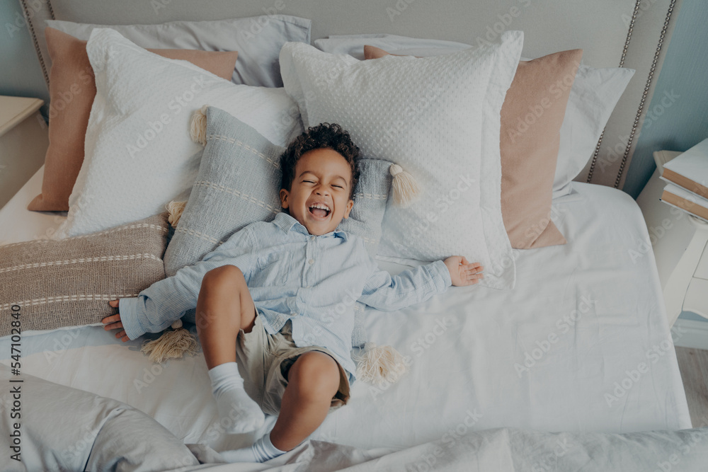 Portrait of afro american joyful little boy on pillows in bed laughing and smiling Portrait of afro american joyful little boy on pillows in bed laughing and smiling