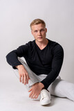 Caucasian blonde model in a black sweater on a white background, sitting on the floor