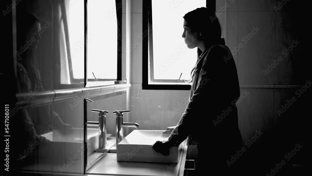 Suffering woman in front of bathroom mirror in mental disorder feeling anxiety in monochromatic