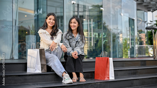 Asian female friends with their shopping bags sitting on the street in front of the shopping mall