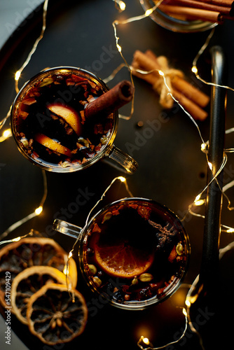 Christmas mulled red wine with spices and oranges on a black table with light garland, traditional hot drink at Christmas, festive cocktail