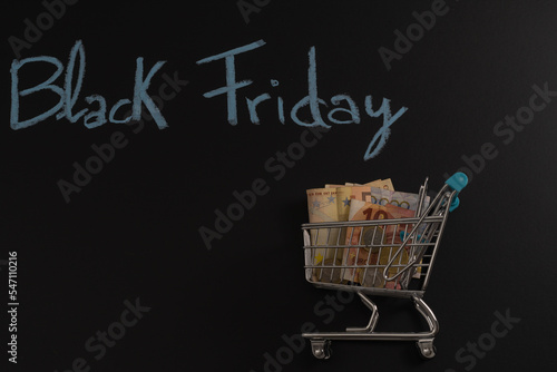 Money inside a shopping cart with Black Friday text on black background