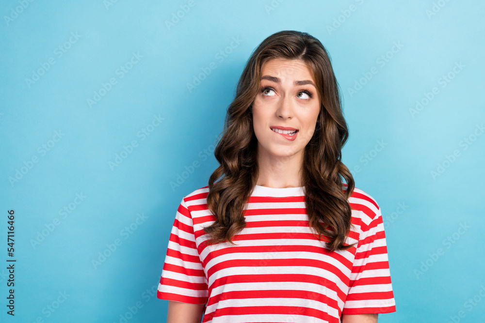 Fototapeta premium Closeup photo of young funny nervous excited pretty lady wear red stiped t-shirt curly hair bite lips looking empty space oops isolated on blue color background