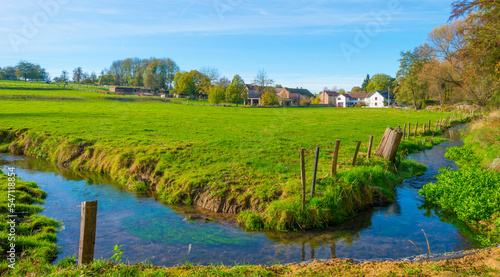 Grassy green edge of a stream through a small village in bright sunlight at fall, Voeren, Limburg, Belgium, November, 2022
