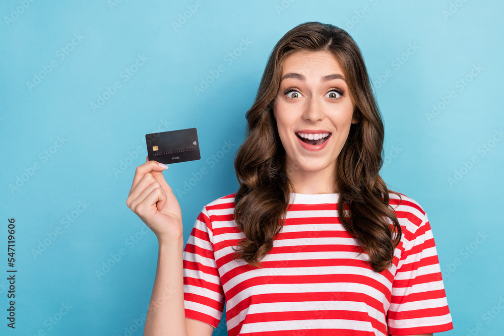 Photo of astonished funny lady customer wear striped stylish clothes showing plastic card recommend use isolated on blue color background Photo of astonished funny lady customer wear striped stylish clothes showing plastic card recommend use isolated on blue color background