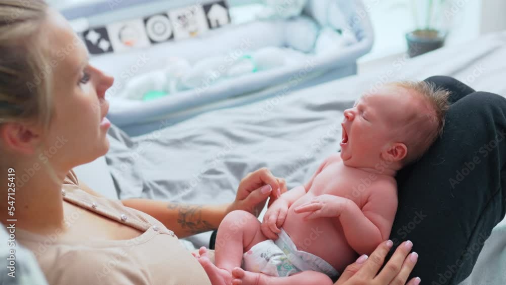 Blond caucasian middle-aged mother in casual clothes sitting on bed with her baby infant on her thighs mocking his big yawn. Sleepy newborn baby boy in diaper. High quality 4k footage Blond caucasian middle-aged mother in casual clothes sitting on bed with her baby infant on her thighs mocking his big yawn. Sleepy newborn baby boy in diaper. High quality 4k footage