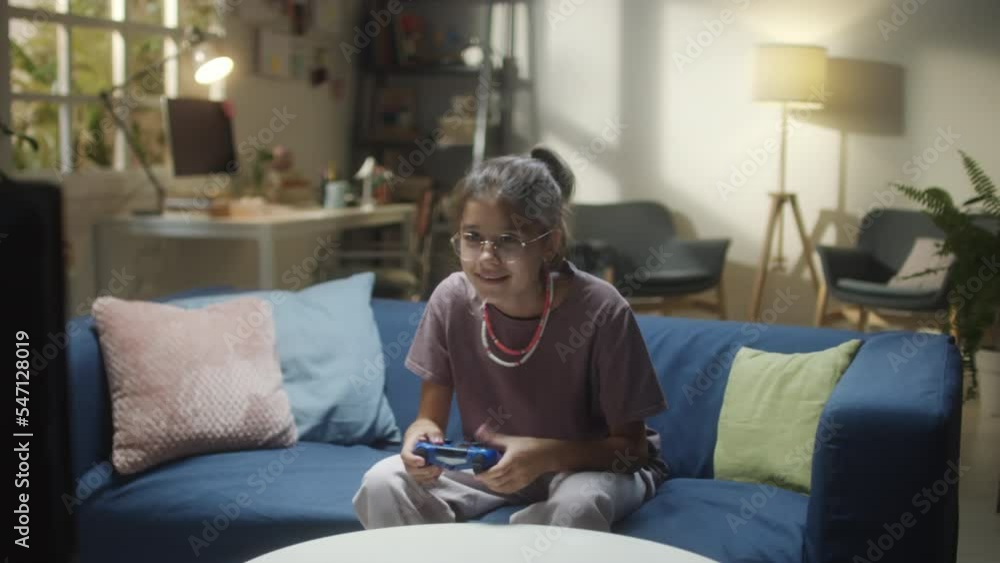 Medium shot of teenage girl sitting on sofa at home and having fun while playing exciting video game Medium shot of teenage girl sitting on sofa at home and having fun while playing exciting video game