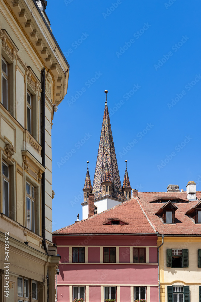 Vertical photo of colourful steeple of Lutheran Cathedral of Saint Mary (Biserica Evanghelica), and iconic eyebrow dormers of Eyes of Sibiu are visible from everywhere, Sibiu, Romania