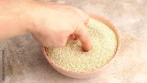 hand stirs quinoa into a ceramic bowl on a brown concrete background, side view, close up