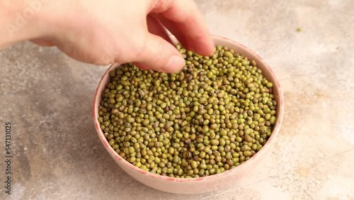 hand stirs mung beans into a ceramic bowl on a brown concrete background, side view, close up