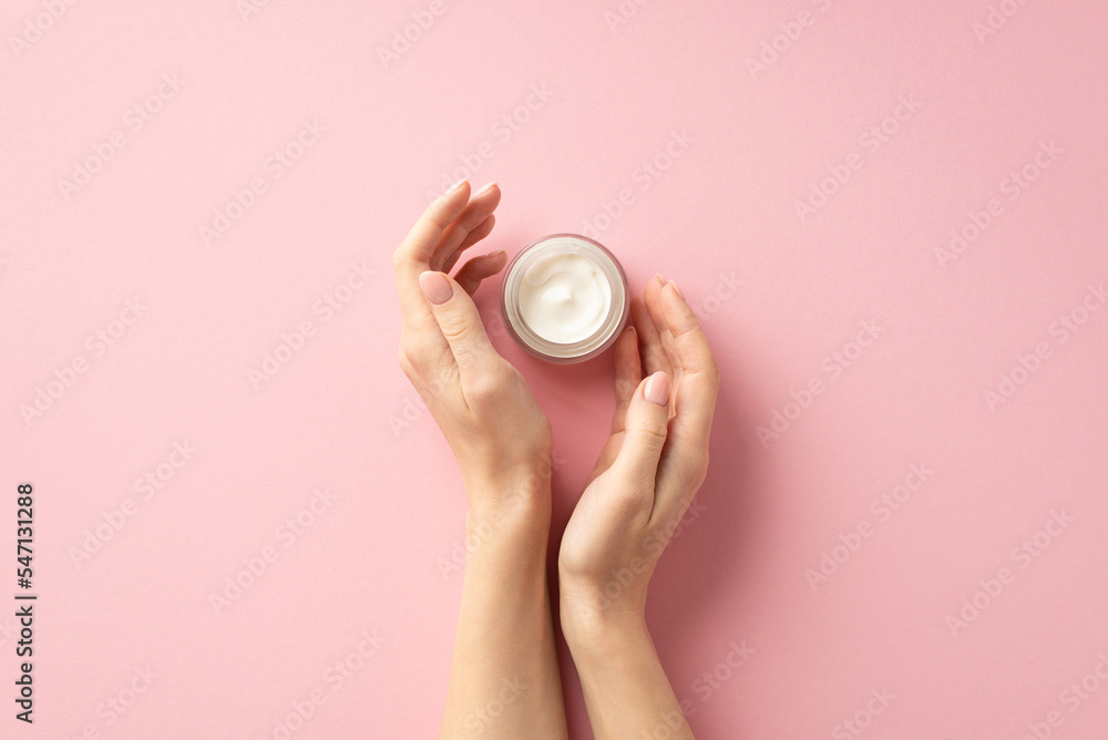 Skin care concept. First person top view photo of young woman's hands and small jar of cream on isolated pastel pink background Skin care concept. First person top view photo of young woman's hands and small jar of cream on isolated pastel pink background