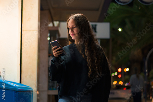 Young woman with her mobile phone walking on the street at night