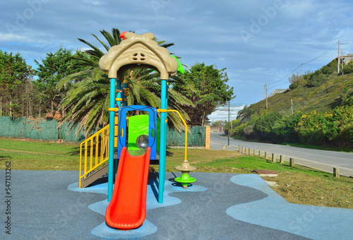 Tobogán colorido de un parque infantil con suelo de caucho azuly detrás una palmera y el mar photo