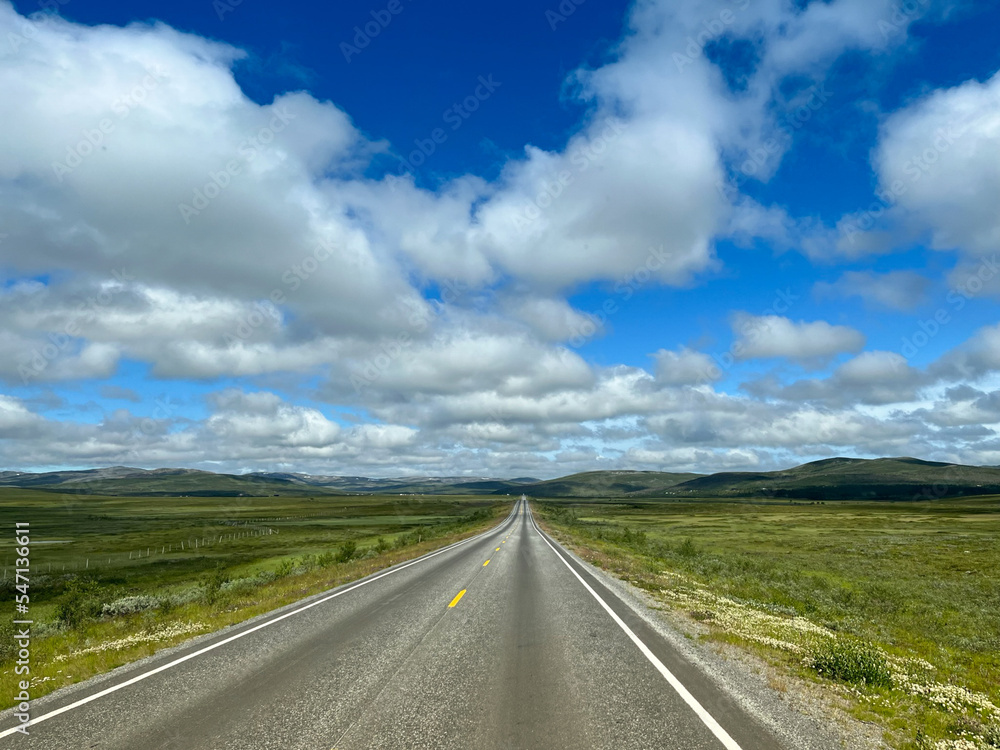 Empty asphalt road through the green field and clouds in blue sky