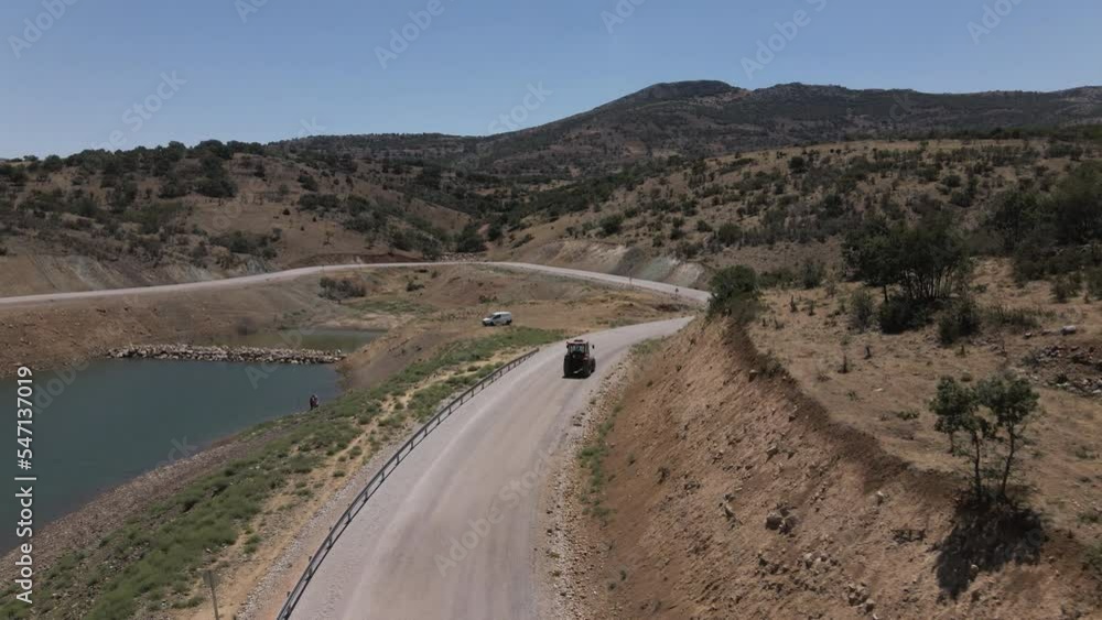 Drone following red trucktor slowly driving a road in turkey karaman between blue lake and mountains at a sunny summer though curves