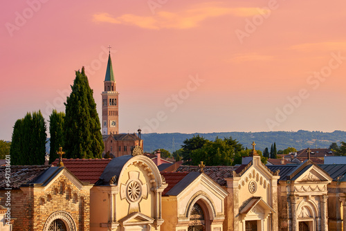 Blick über einen Friedhof in Pieve di Soligo im letzen Abendlicht . Im Hintergrund der Kirchturm von Parrocchia del Duomo Santa Maria Assunta