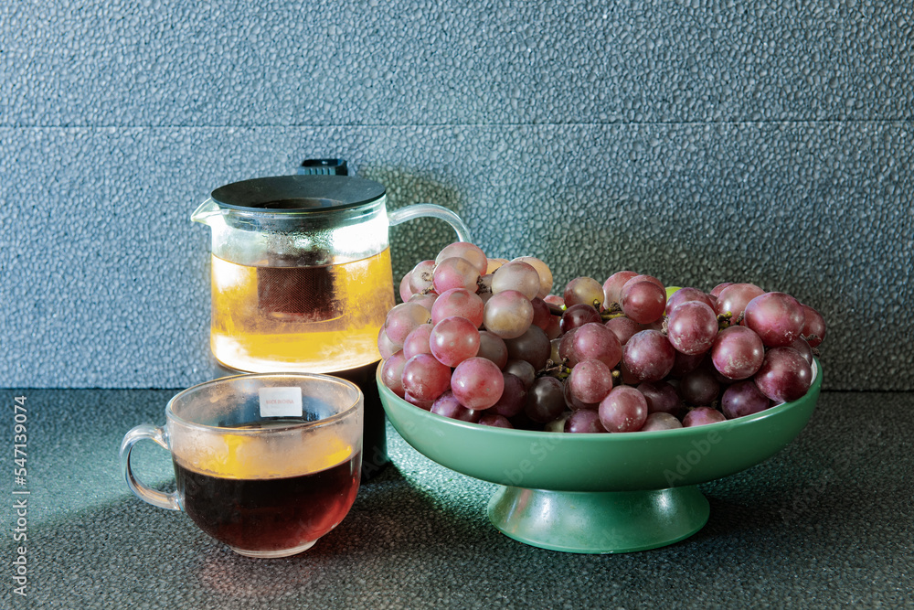 Purple grapes and teapots and cups of tea on a black background on a plate Purple grapes and teapots and cups of tea on a black background on a plate