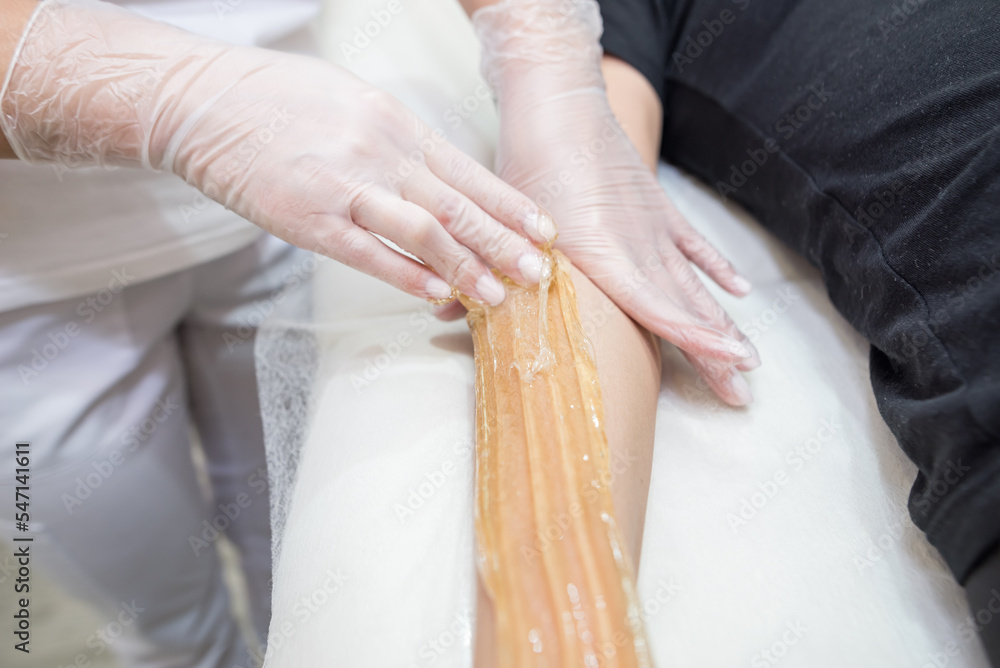 Obraz premium Cosmetologist applies sugar paste to the hand of a young woman.Depilation of female hands in a beauty parlor.