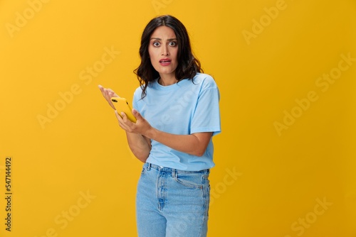 Woman blogger with a phone in her hands in a blue t-shirt and jeans on a yellow background smile signs gestures symbols  online communication and video call  copy space  free background