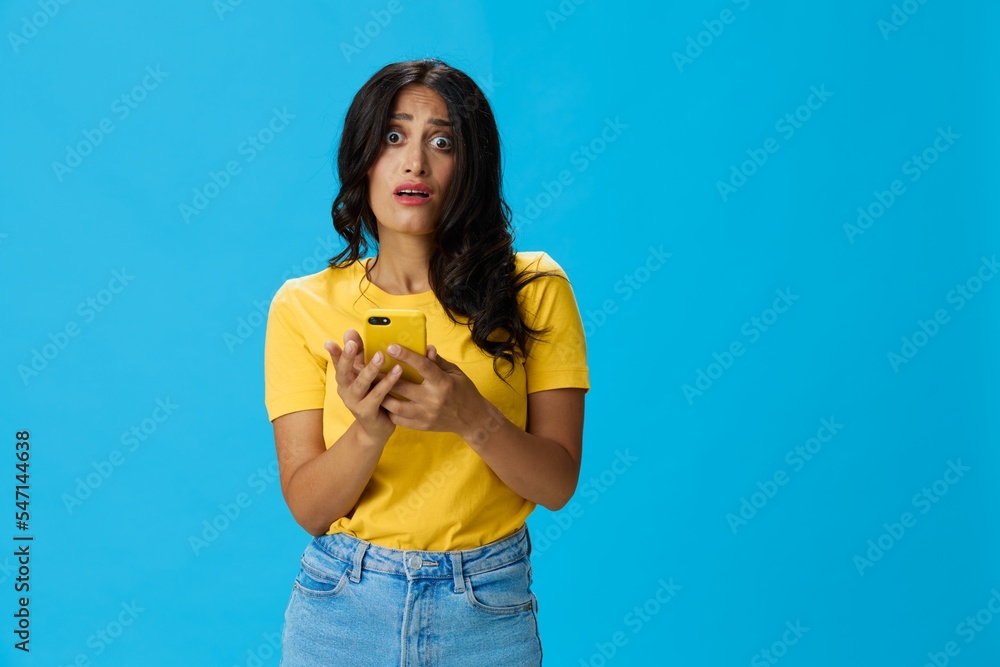 Woman with a phone in her hands with a yellow case on a blue background in a yellow T-shirt, emotions signals gestures, online lifestyle concept, shopping, communication, learning, business online Woman with a phone in her hands with a yellow case on a blue background in a yellow T-shirt, emotions signals gestures, online lifestyle concept, shopping, communication, learning, business online