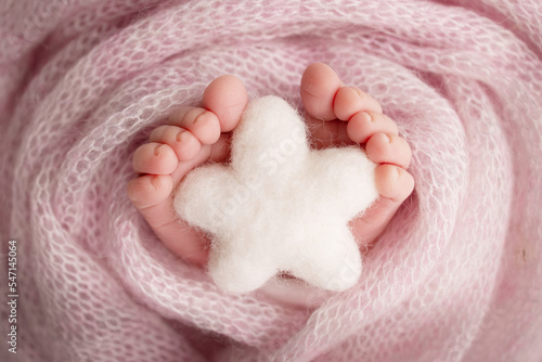 Knitted white star in the legs of a baby. Soft feet of a new born in a pink wool blanket. Close-up of toes, heels and feet of a newborn. Macro photography the tiny foot of a newborn baby.  © Vad-Len