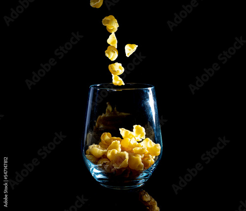 raw pasta in glass jar, wine glass. in bucket. raw pasta on black background. front view raw pasta, dropped from hand, place for text, yellow long spaghetti straws,